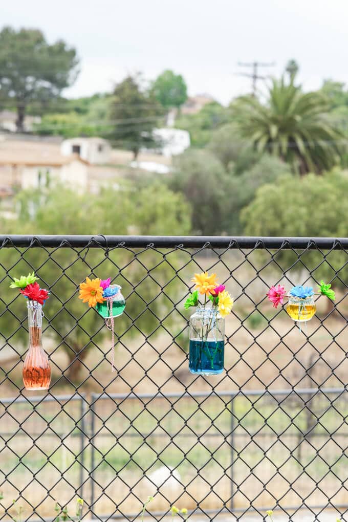 Flowers along a fence line with colored water make a pretty, casual party backdrop (perfect for a festive baby shower, too!)
