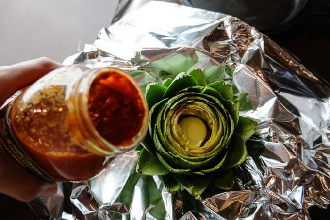How to make easy Italian oven-roasted artichokes with three ingredients. Just pour some premade sauce over and cook. The flavors will seep in and the result is WAY better than boiling.