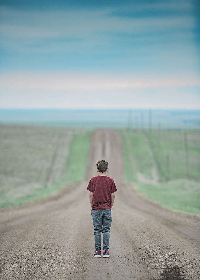 Boy standing in the middle of a long road