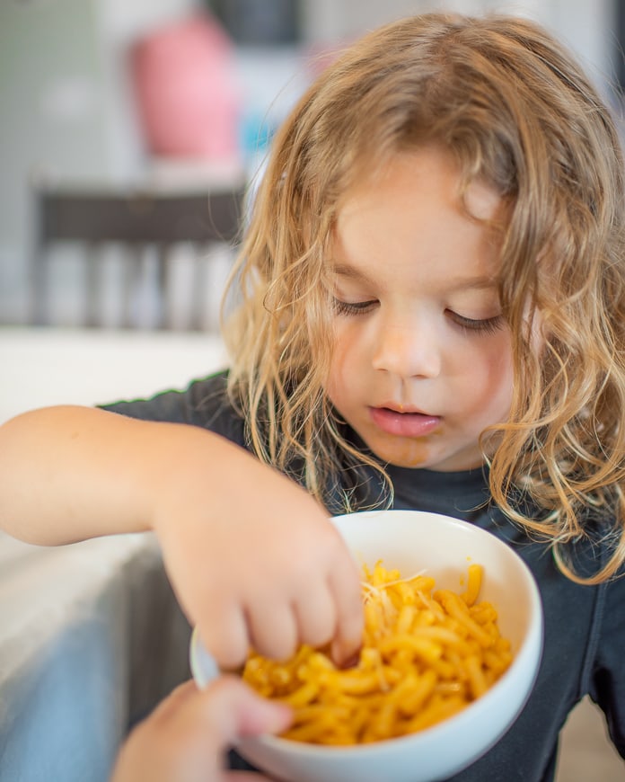 Preschooler eating macaroni and cheese without a fork