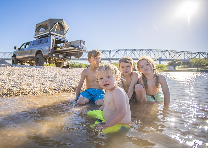 Four brothers swimming in Texas river next to powerstroke and rooftop tent