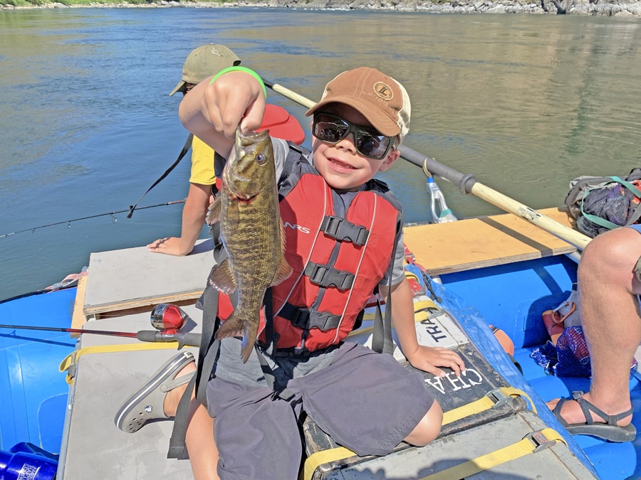 Little boy catching small mouth bass while american white water rafting on the snake river
