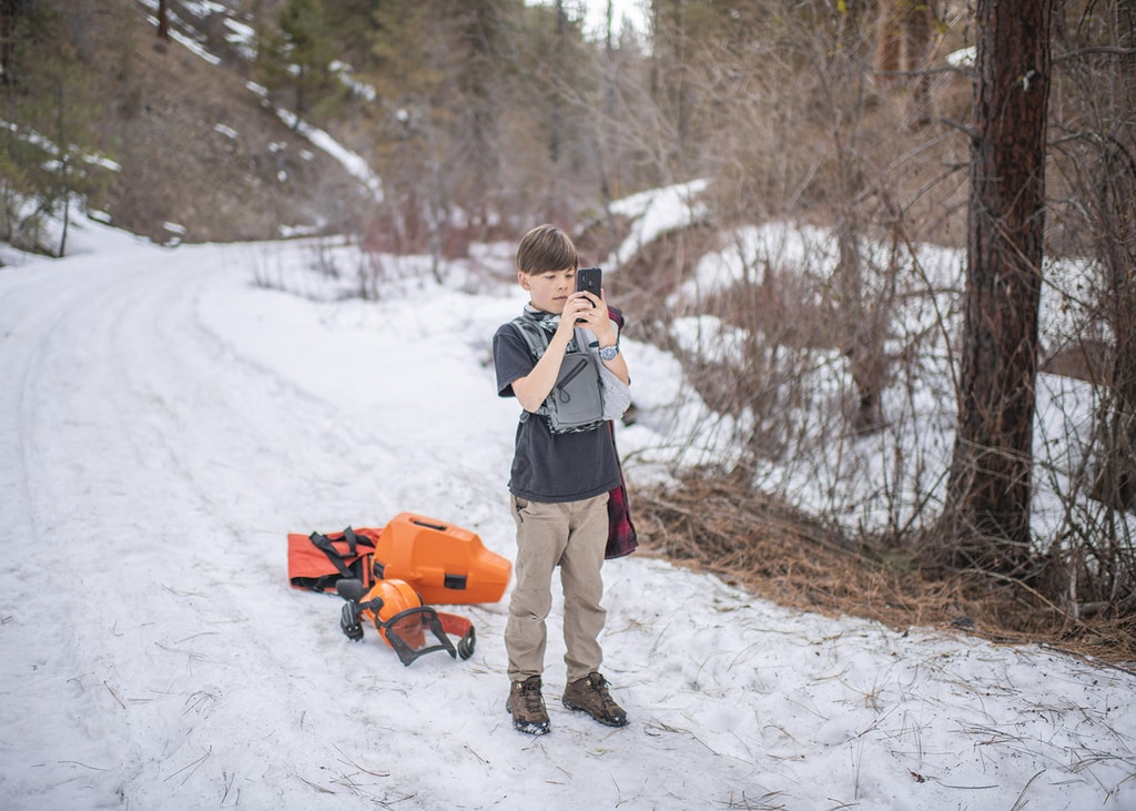 Little boy olin taking pictures in snow next to stihl chainsaw truck gear