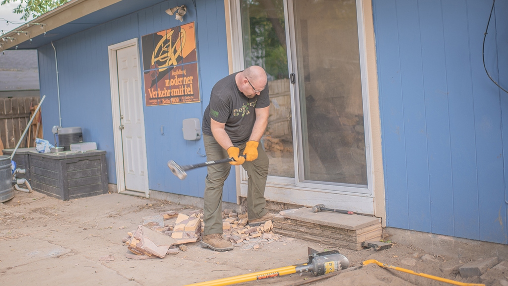 Nate Day using a sledge hammer to knock out an old brick stairs